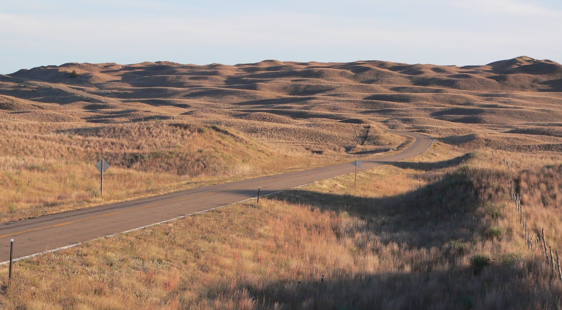 A two-lane road curving through the Sandhills' rolling grass-covered dunes in low evening sun